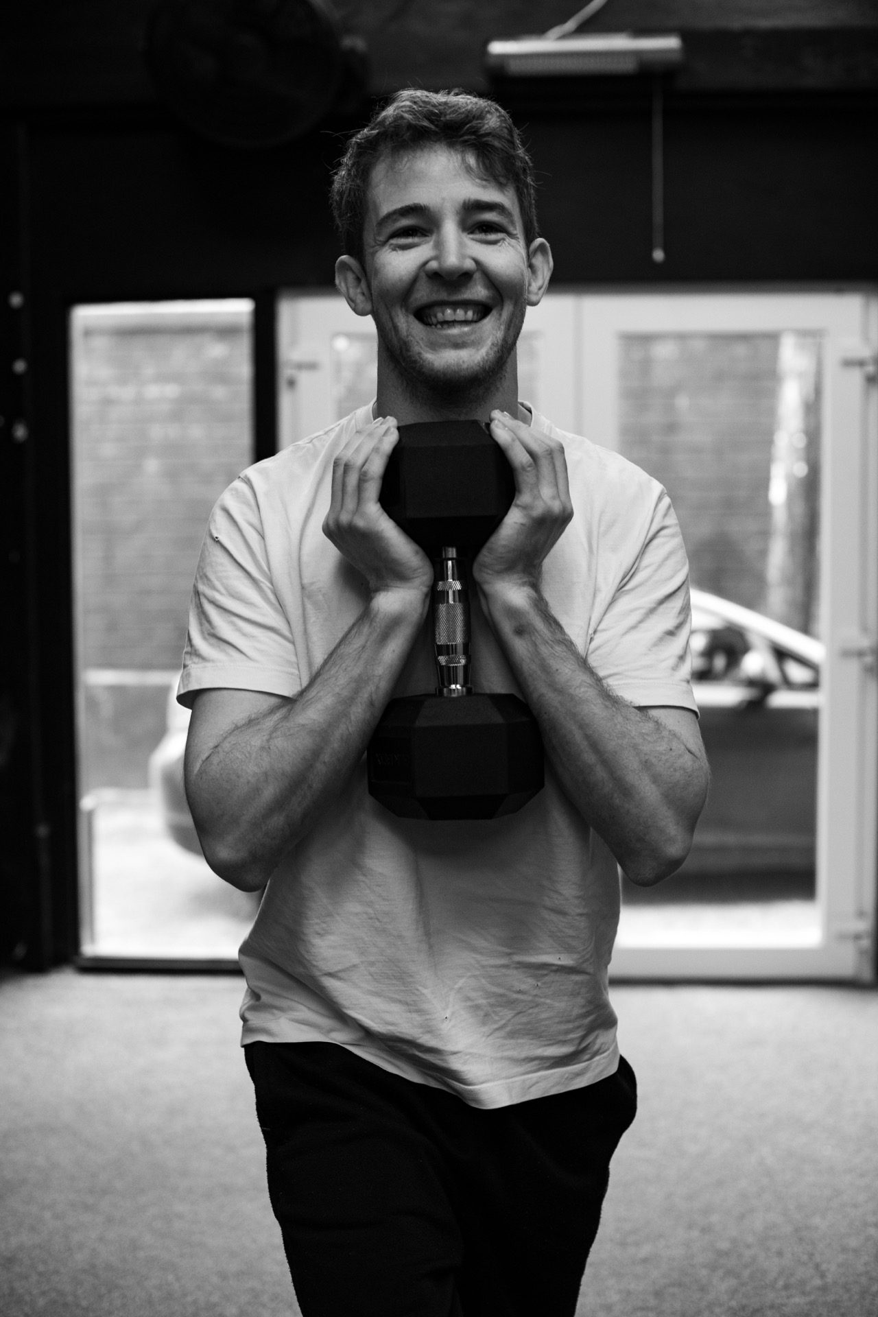 A Dark Horse member smiling, holding a dumbbell at chest level after a set.